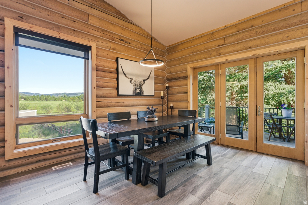 Dining area featuring log-style wood walls, a vaulted ceiling, and wood-finish flooring