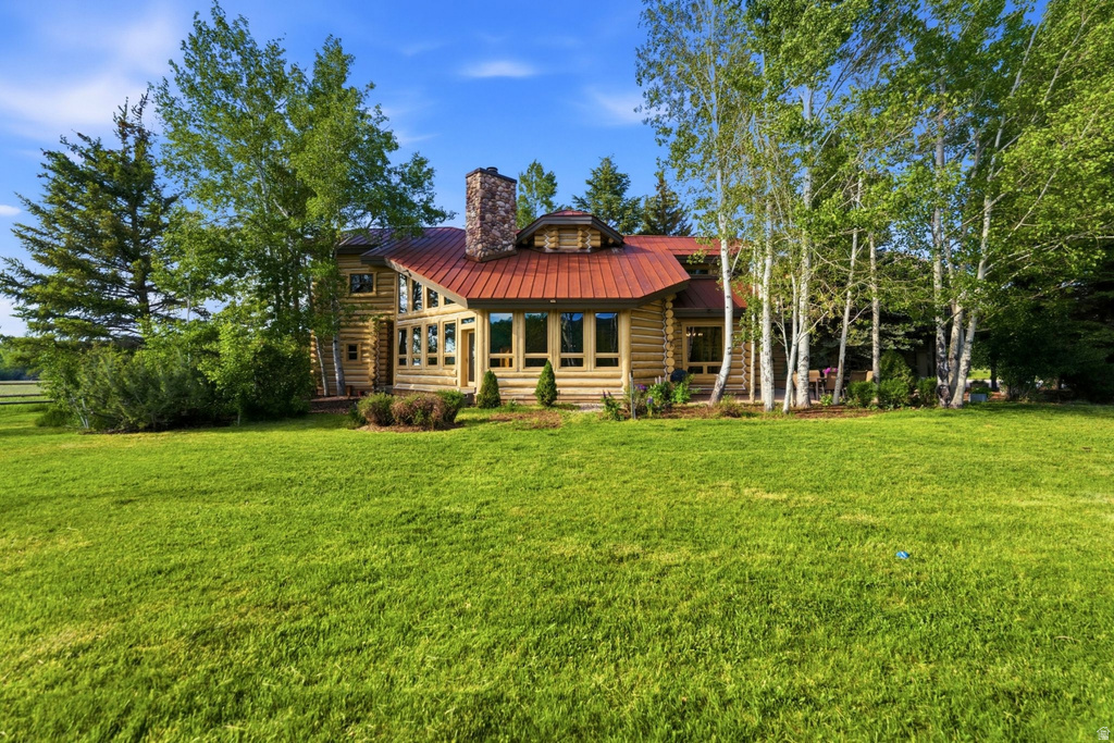 Log home exterior featuring a red metal roof, stone chimney, and expansive window arrangement