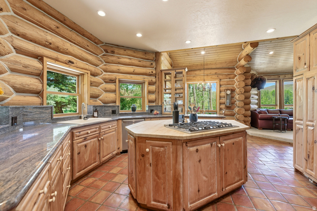 Log cabin style kitchen featuring wood-finish cabinetry, natural stone countertops, a central island with an integrated cooktop, and terracotta-style flooring