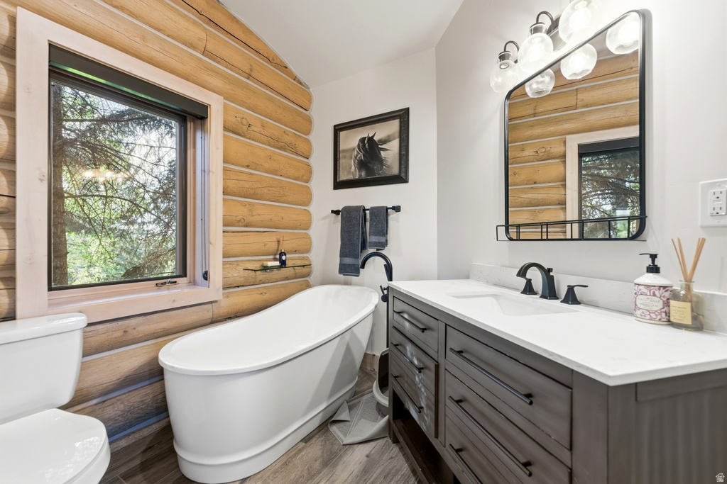 Bathroom featuring log walls, a freestanding soaking tub, a single window, a double vanity with a white countertop, and wood-finish flooring