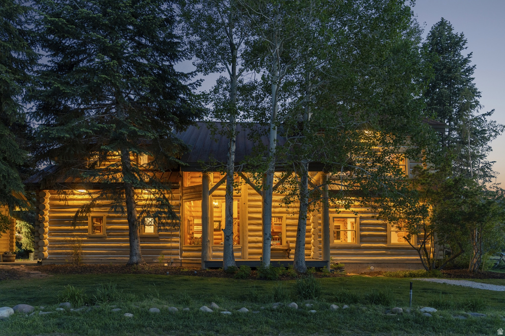 Log cabin exterior featuring a covered porch, multiple windows, and surrounding mature trees
