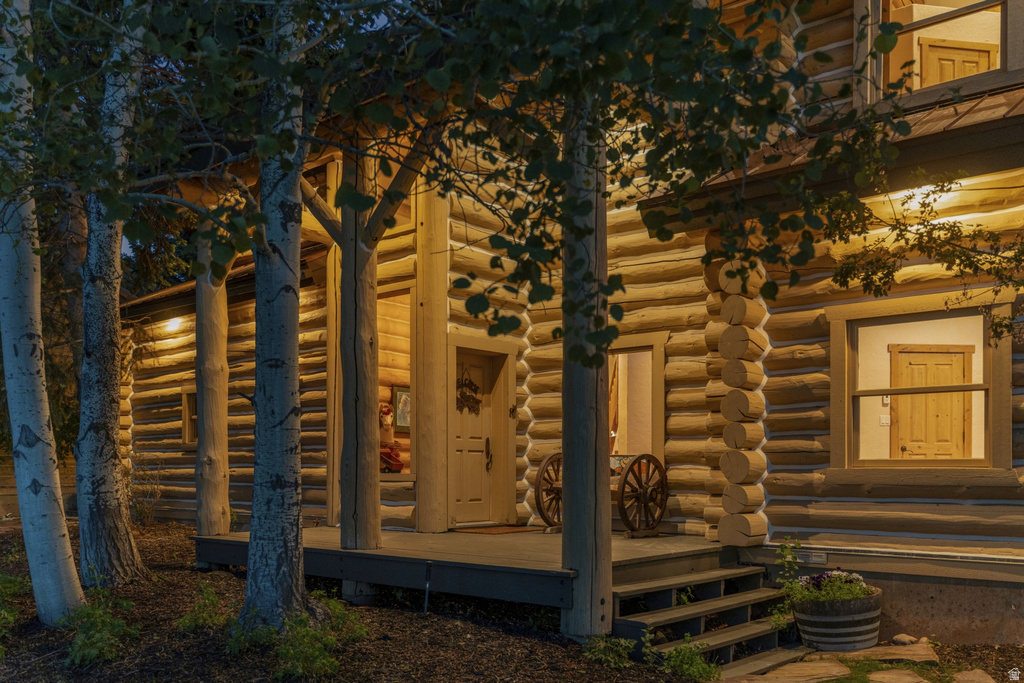 Log cabin exterior featuring a covered porch, natural wood log siding, and visible interior wood doors through windows