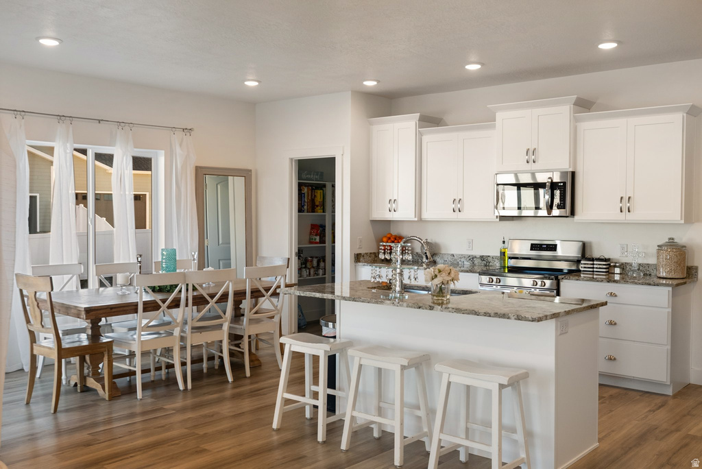 Kitchen and dining area featuring white cabinetry, stainless steel appliances, a center island with bar seating, granite countertops, and wood-finish flooring