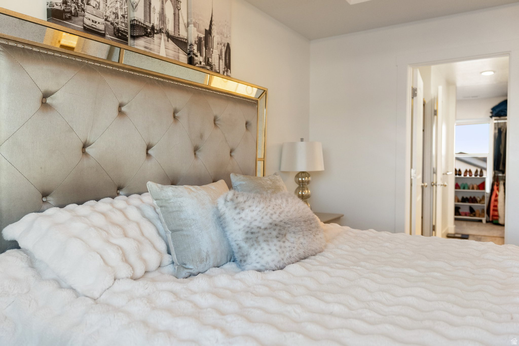 Spacious room featuring a tufted fabric headboard with mirror trim, white walls, and an open doorway revealing a closet with built-in shelving