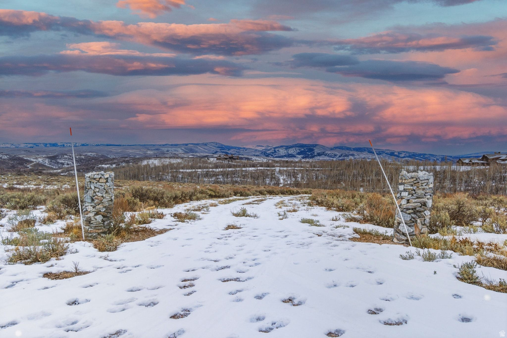 Expansive property featuring a snow-dusted natural landscape, distant mountain ranges, and two stacked stone entry pillars