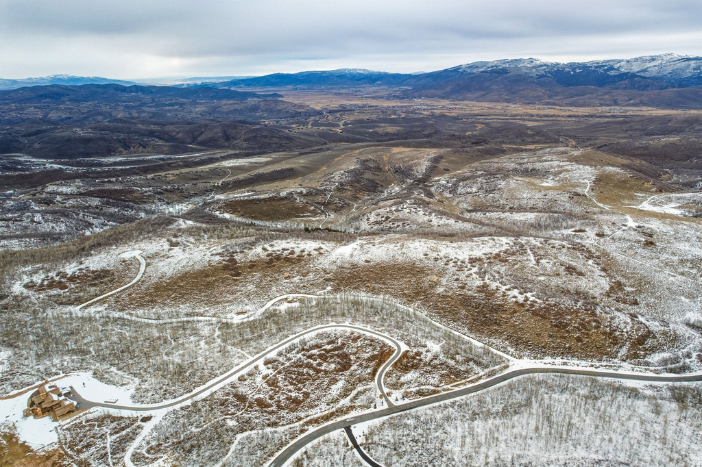 Sweeping mountain terrain with a snow-dusted landscape, featuring winding roads and distant peaks under a cloudy sky