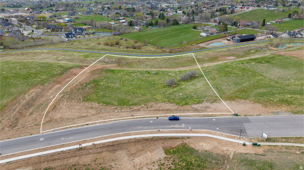 Expansive lot featuring a curvilinear paved road, concrete sidewalk, gentle slopes, and existing vegetation