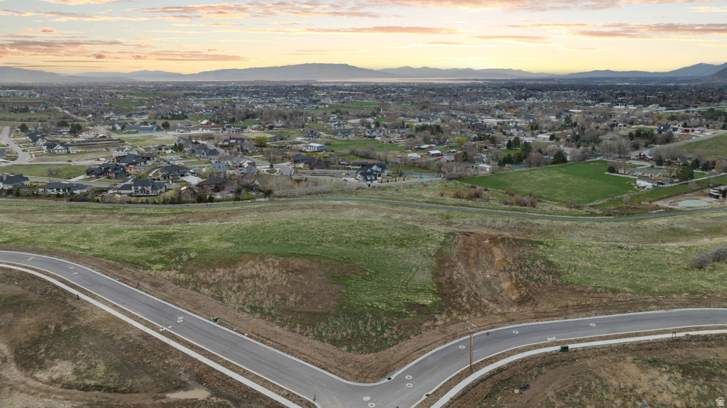 Expansive undeveloped land featuring a paved road with concrete sidewalks, established infrastructure, and distant residential areas
