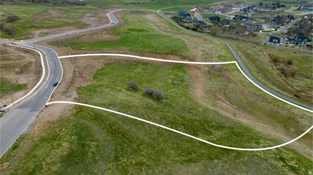 Expansive undeveloped lot featuring a paved road, established curb, green landscape, and mature trees