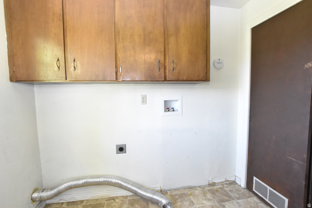 Utility space with wood-finish upper cabinetry, white walls, and vinyl flooring