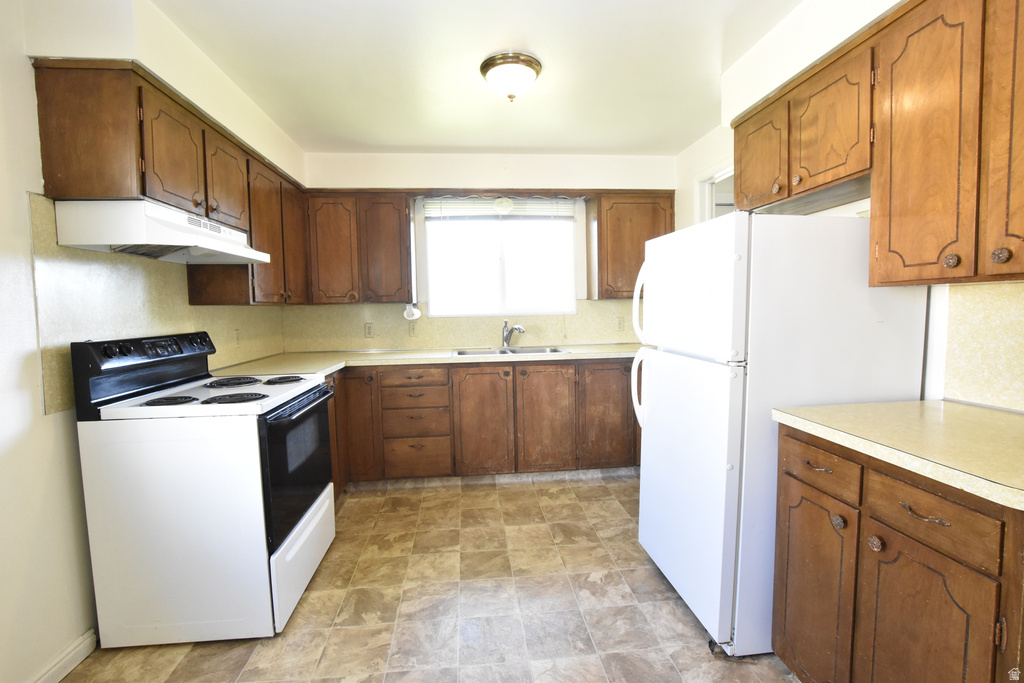 Kitchen featuring wood-finish cabinetry, white appliances, and a window above the sink