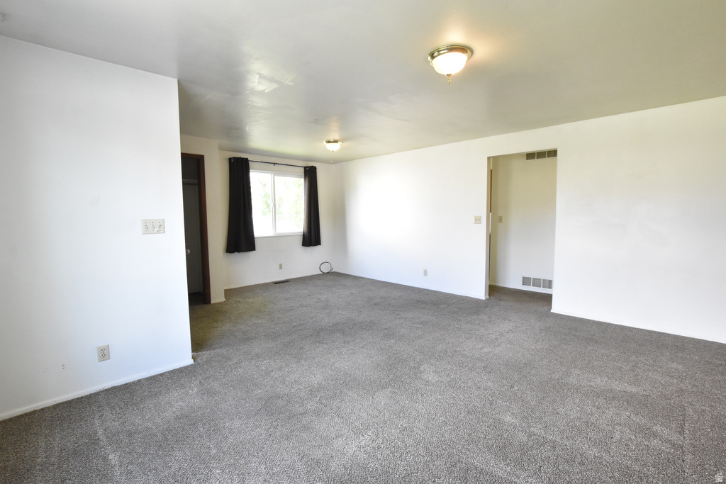 Spacious room featuring gray carpet, white walls, and a large window with black window treatments