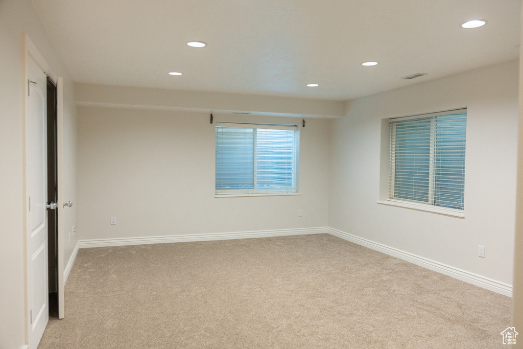 Recessed lighting illuminates the carpeted flooring and white walls, featuring two windows with blinds