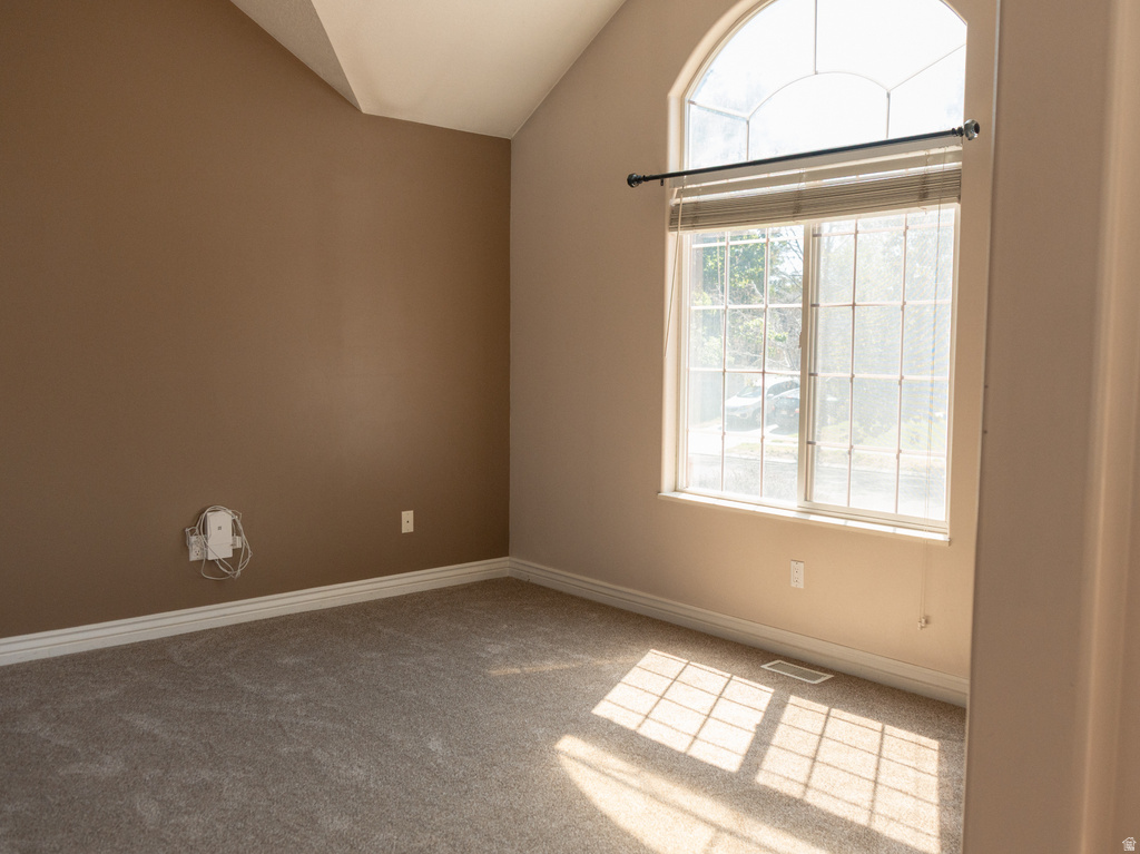 Room featuring vaulted ceilings, arched transom window, large window with blinds, light-toned carpet flooring, and neutral wall paint