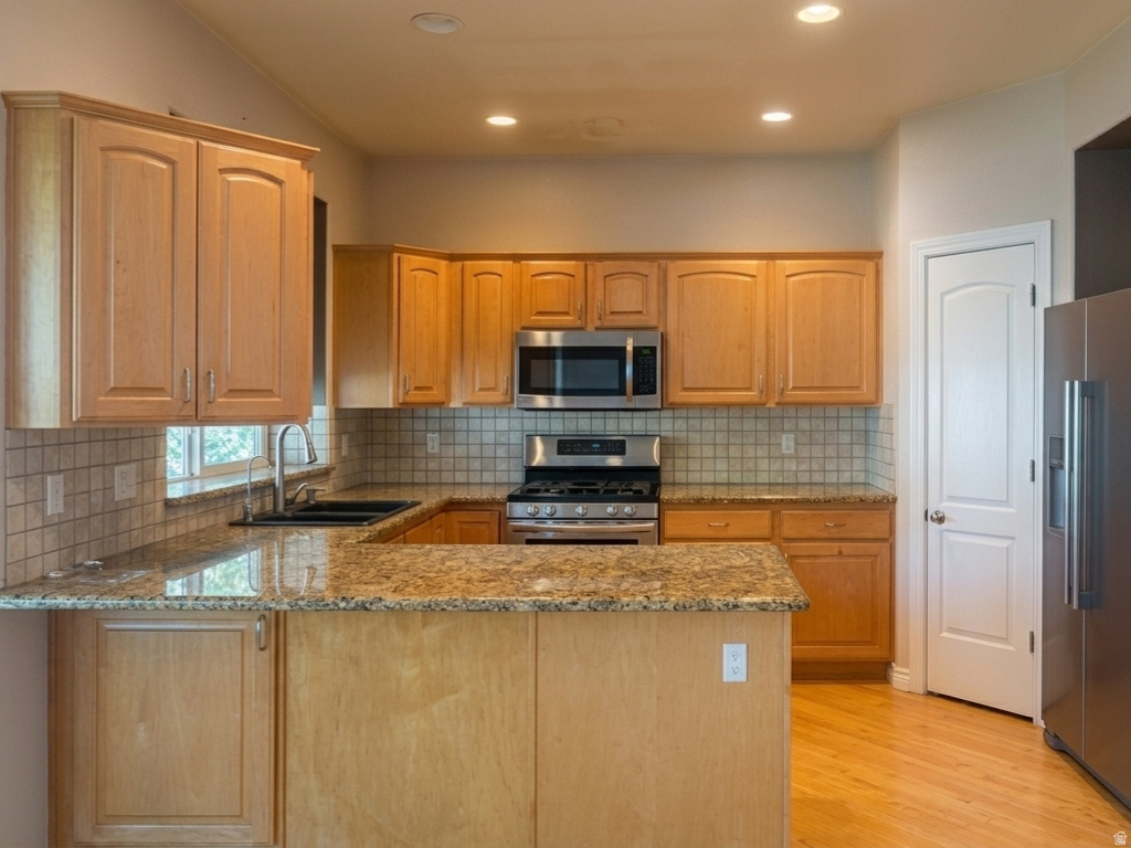 Kitchen featuring light wood cabinetry, granite countertops, stainless steel appliances, tile backsplash, and wood-finish flooring