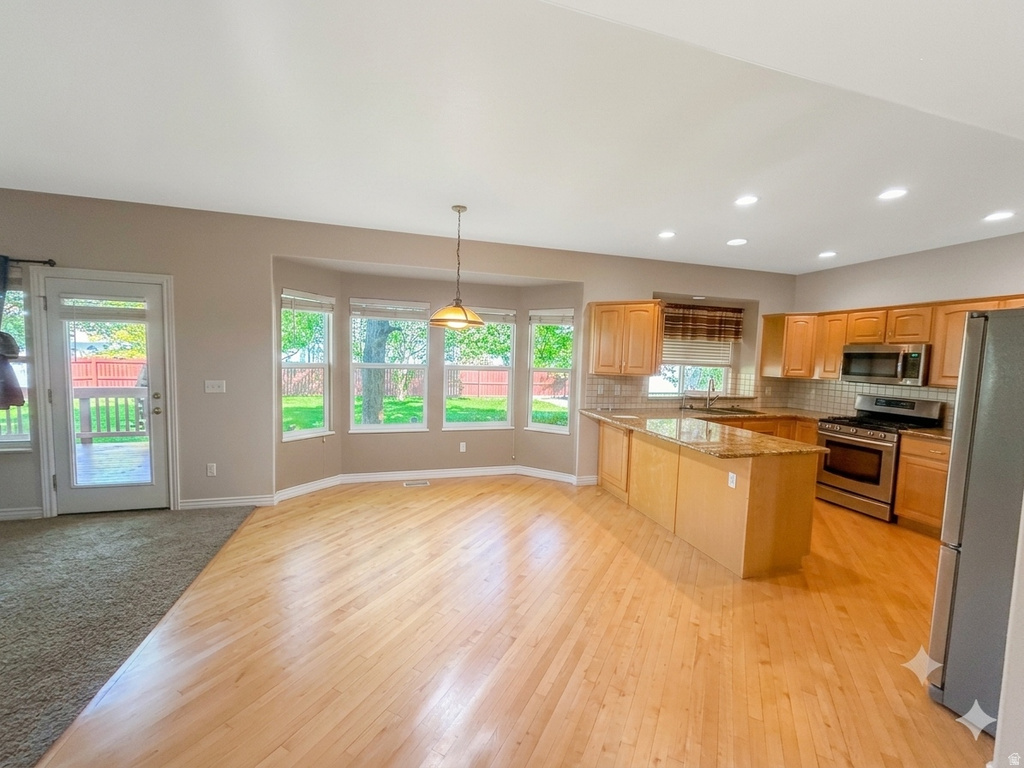 Open-concept kitchen and dining area featuring wood-finish flooring, a kitchen island with stone countertop, stainless steel appliances, and ample natural light from bay windows and a glass-paned door