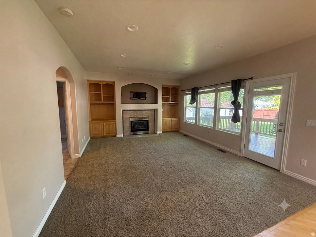 Living area featuring a textured carpet, a fireplace with a tiled surround and mantel, and built-in cabinetry