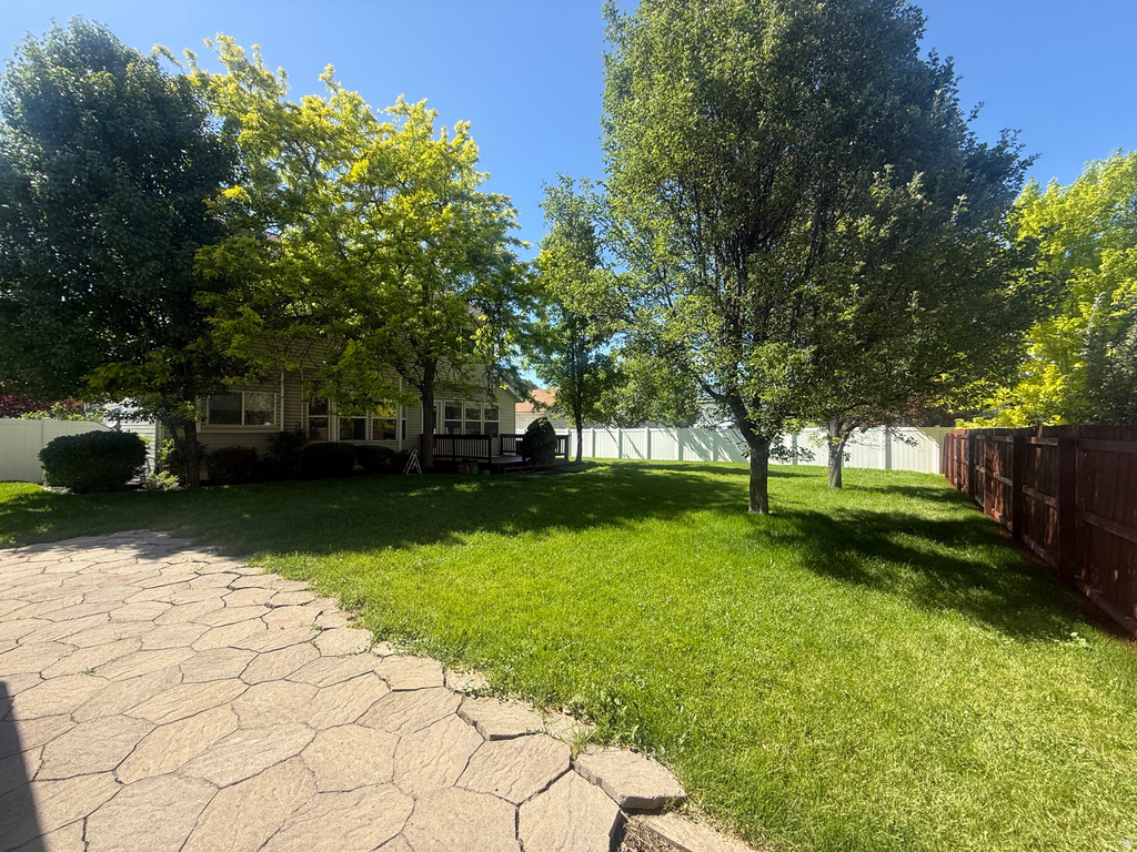 Expansive backyard featuring a large grass lawn, mature trees, a multi-tone paver patio, a wood deck, and perimeter fencing