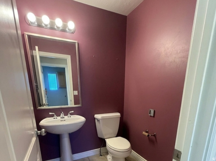 Powder room featuring a pedestal sink, white toilet, and a wall-mounted mirror with overhead lighting