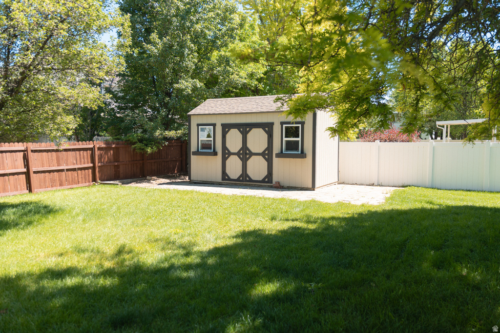 Spacious backyard featuring a storage shed with decorative doors, a brown privacy fence, a white vinyl fence, and mature trees