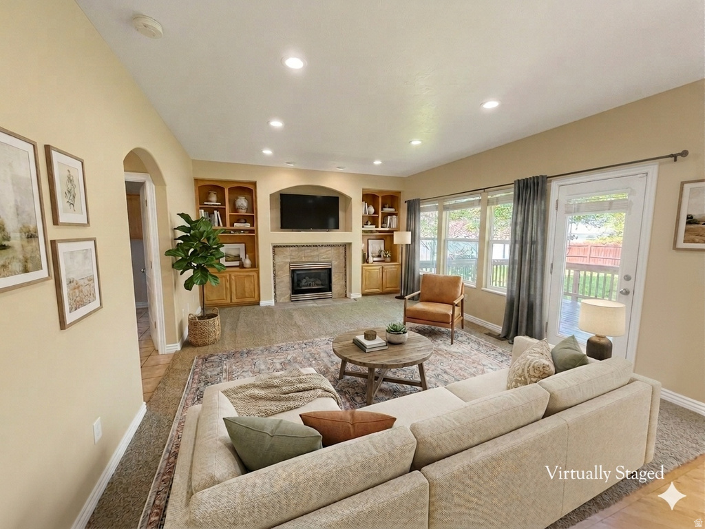Living area featuring a fireplace with a stone surround, built-in wooden shelving, recessed lighting, and large windows