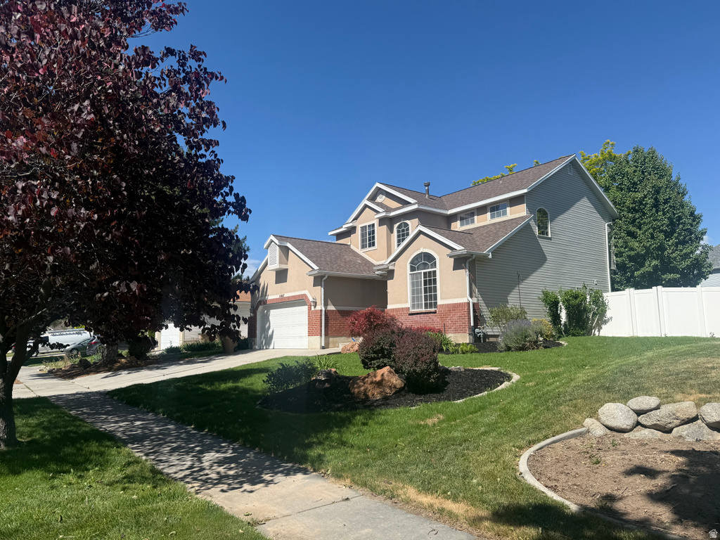 Two-story property featuring a stucco and brick exterior, arched windows, an attached two-car garage, established front landscaping, and a side-yard privacy fence