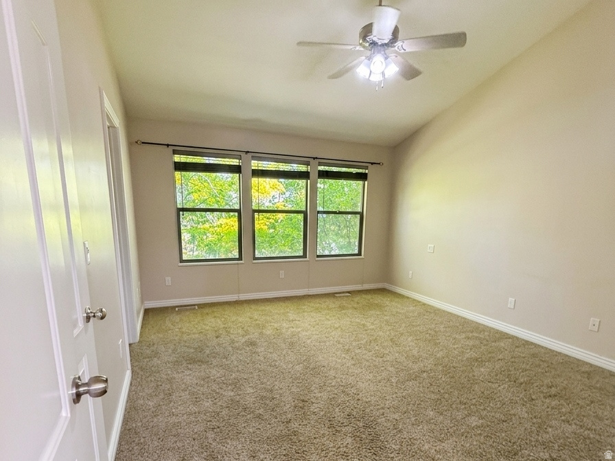 Spacious interior room featuring plush carpeting, three large windows, a ceiling fan with integrated lighting, and white paneled doors