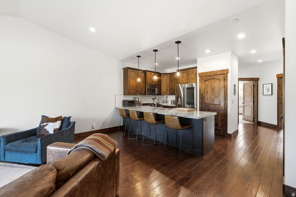 Open-concept kitchen featuring dark wood cabinetry, stainless steel appliances, a center island with bar seating, and pendant lighting