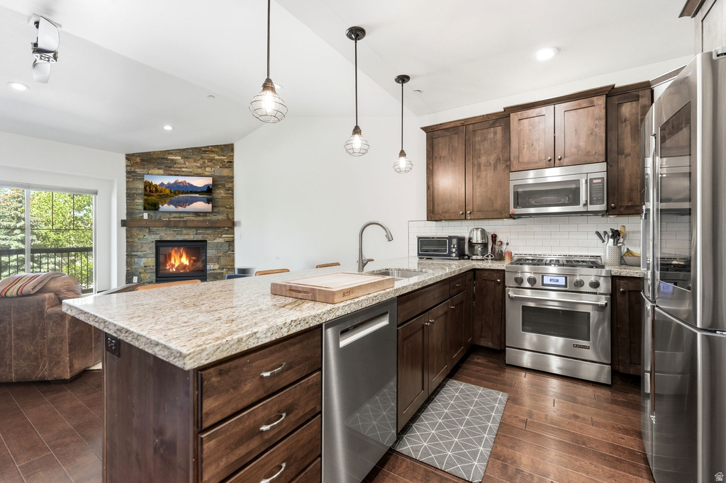 Kitchen with granite countertops, stainless steel appliances, dark wood cabinetry, and wood-finish flooring