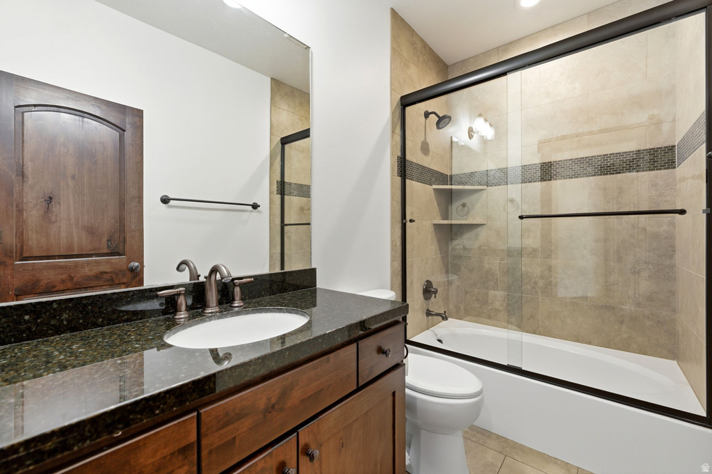 Bathroom featuring a vanity with dark wood cabinetry and a dark stone countertop, an undermount sink with bronze-finish fixtures, and a shower-over-tub with sliding glass doors