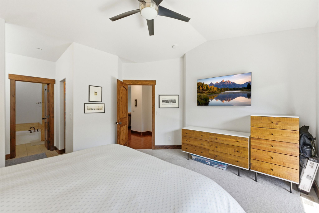 Carpeted bedroom featuring a ceiling fan, vaulted ceiling, and wood-trimmed doorways