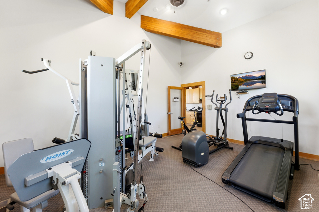 Dedicated fitness room featuring vaulted ceilings with exposed wood beams, a mounted television, and carpet flooring