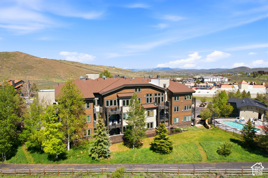 Multi-story building featuring balconies with dark railings, a brown shingled roof, and a stone facade