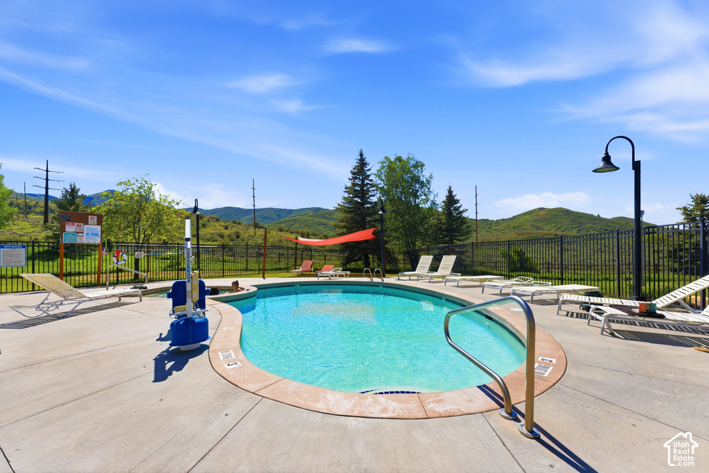 Freeform swimming pool with a concrete surround, metal perimeter fencing, and distant mountain scenery