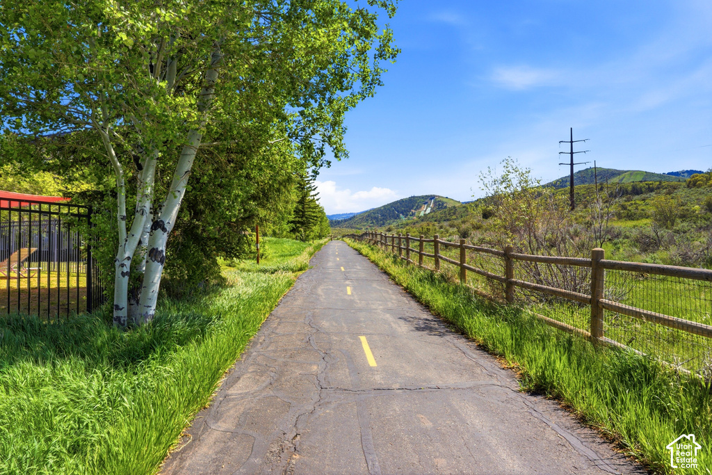 Paved pathway bordered by a rustic wood fence, mature trees, and natural green landscaping