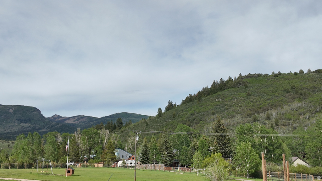 Expansive green field with natural landscaping, surrounded by mature trees and distant mountain ranges