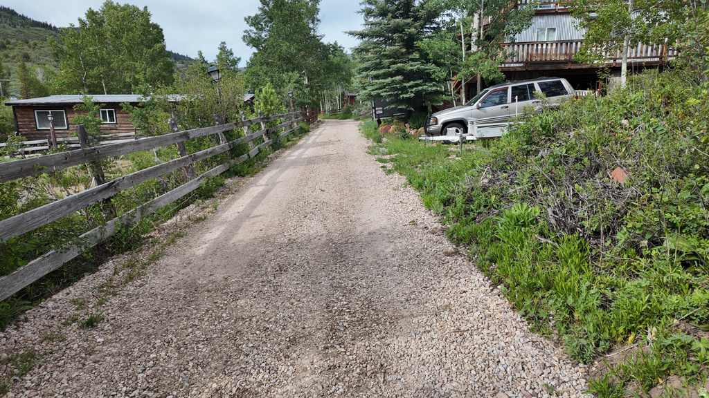 Gravel drive leading to a multi-level structure with a wood deck and surrounding mature trees