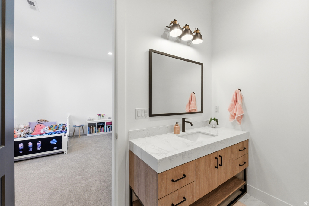 Bathroom vanity featuring a light wood-finish cabinet with black hardware, a white countertop, and an undermount sink