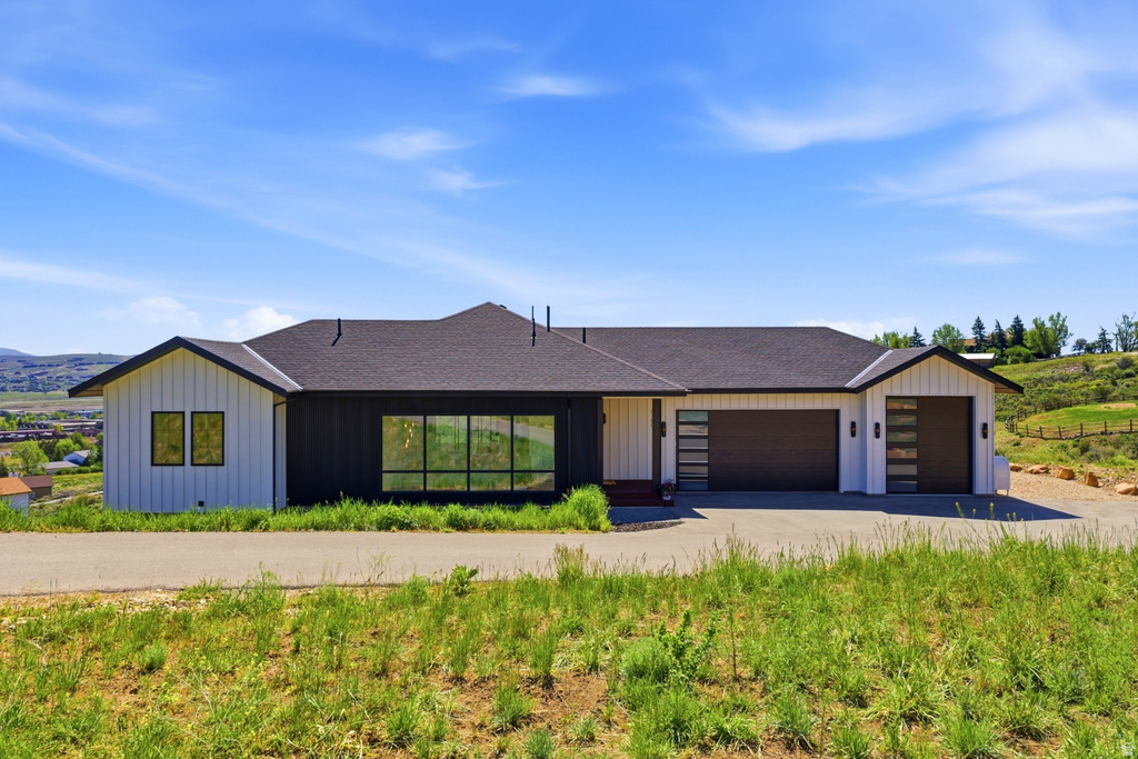 Modern ranch-style home featuring a dark shingle roof and a contrasting exterior of white vertical siding and black horizontal siding