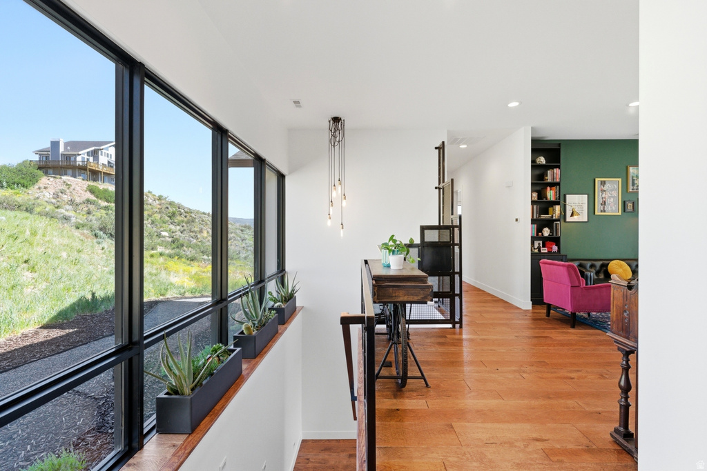 Expansive window wall with black frames, hardwood flooring, recessed lighting, built-in shelving, and a multi-pendant light fixture