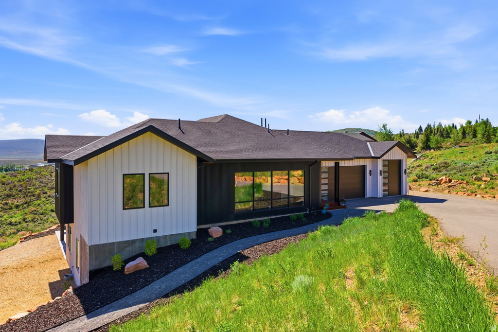 Contemporary exterior featuring white board-and-batten siding with dark trim, expansive windows, a dark shingle roof, and a two-car garage with modern doors