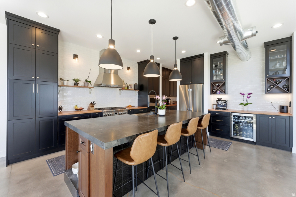 Spacious kitchen featuring an oversized island with seating, dark shaker cabinetry, stainless steel appliances, and a dedicated beverage refrigerator