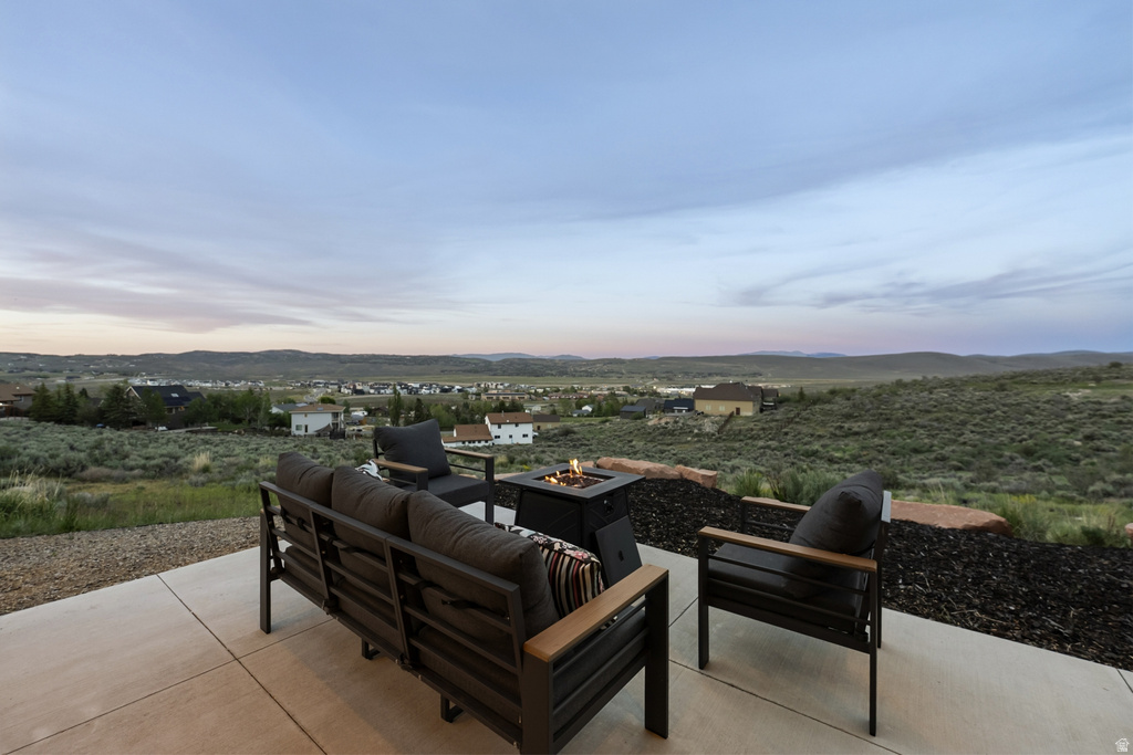 Concrete patio with a built-in fire pit, surrounded by natural landscaping and distant architectural structures