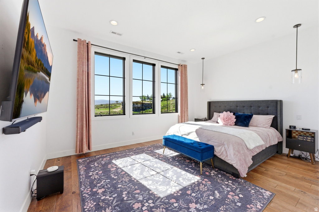 Spacious bedroom featuring hard-surface flooring, multiple large windows with black framing, recessed lighting, and wall-mounted pendant lights