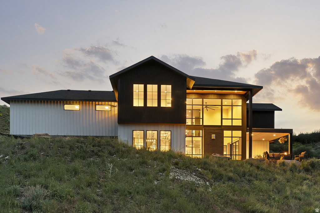 Modern architectural design featuring expansive window walls, a covered outdoor patio, a dark-pitched roof, and white vertical siding