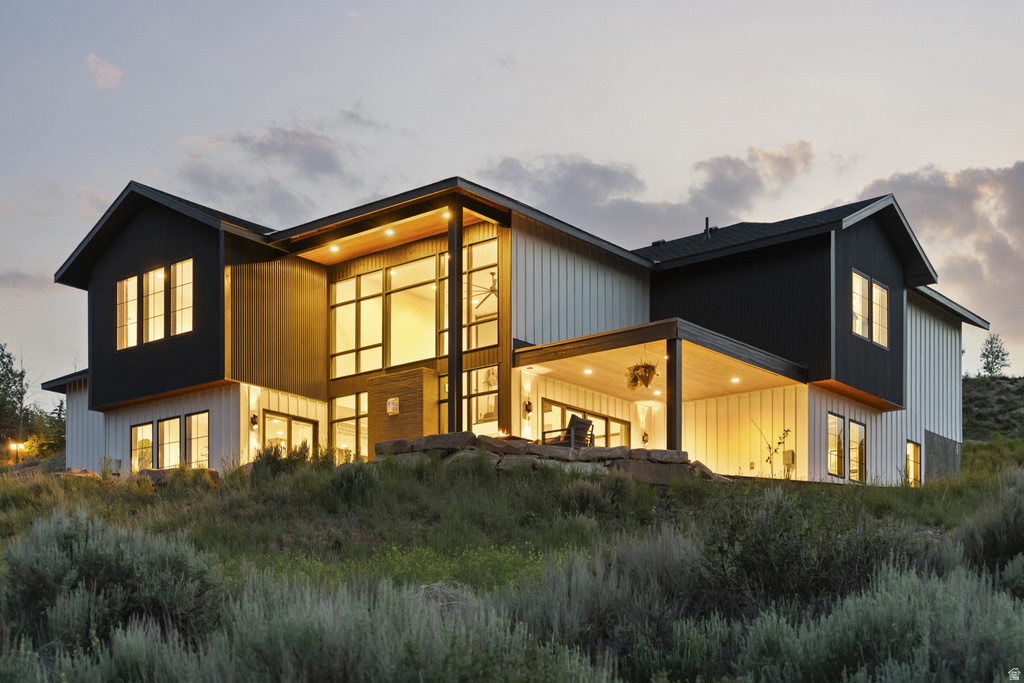 Modern exterior featuring a prominent two-story window wall, covered patio, dark vertical siding, light vertical siding, and a sloped terrain