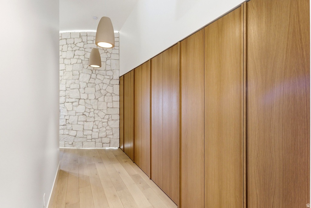 Hallway featuring warm wood-finish flooring, full-height wood-panel storage, and a stone accent wall