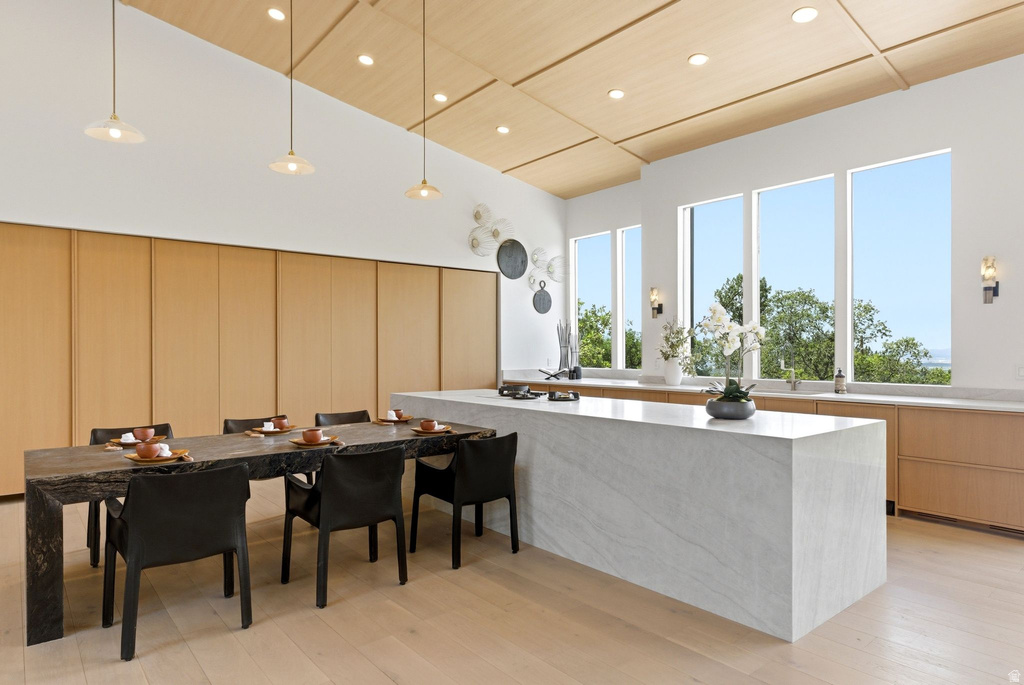 Sleek kitchen and dining area featuring a waterfall island, light wood-finish flooring, a long dining table, built-in cabinetry, and multiple large windows