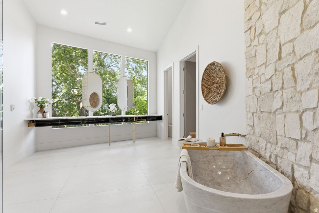 Spacious bathroom featuring a freestanding stone soaking tub, a full-height stone accent wall, and expansive windows