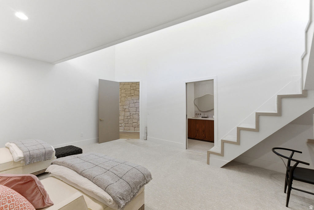 Open concept living space featuring a high ceiling, recessed lighting, carpet flooring, a floating staircase with light wood-finish treads, and a doorway leading to a room with stone walls